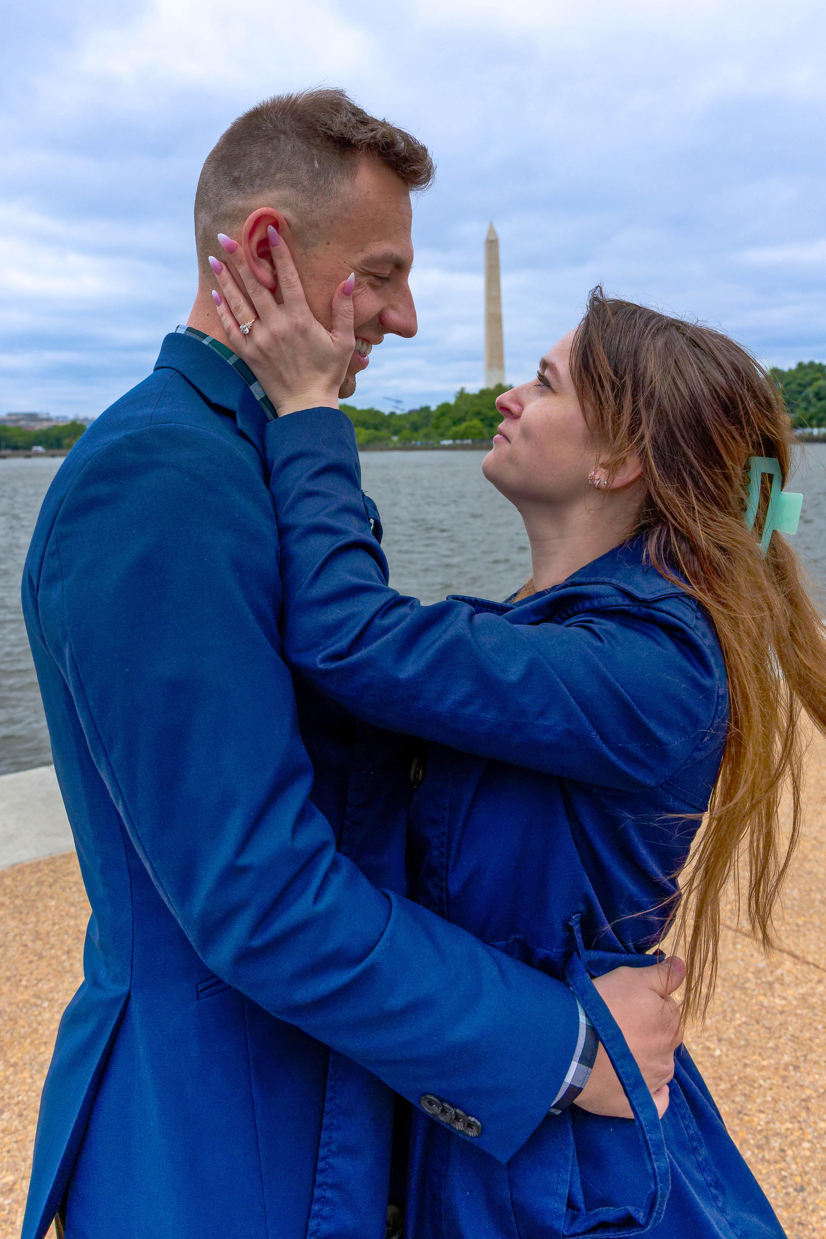 A couple embracing by the Tidal Basin with the Washington Monument behind them